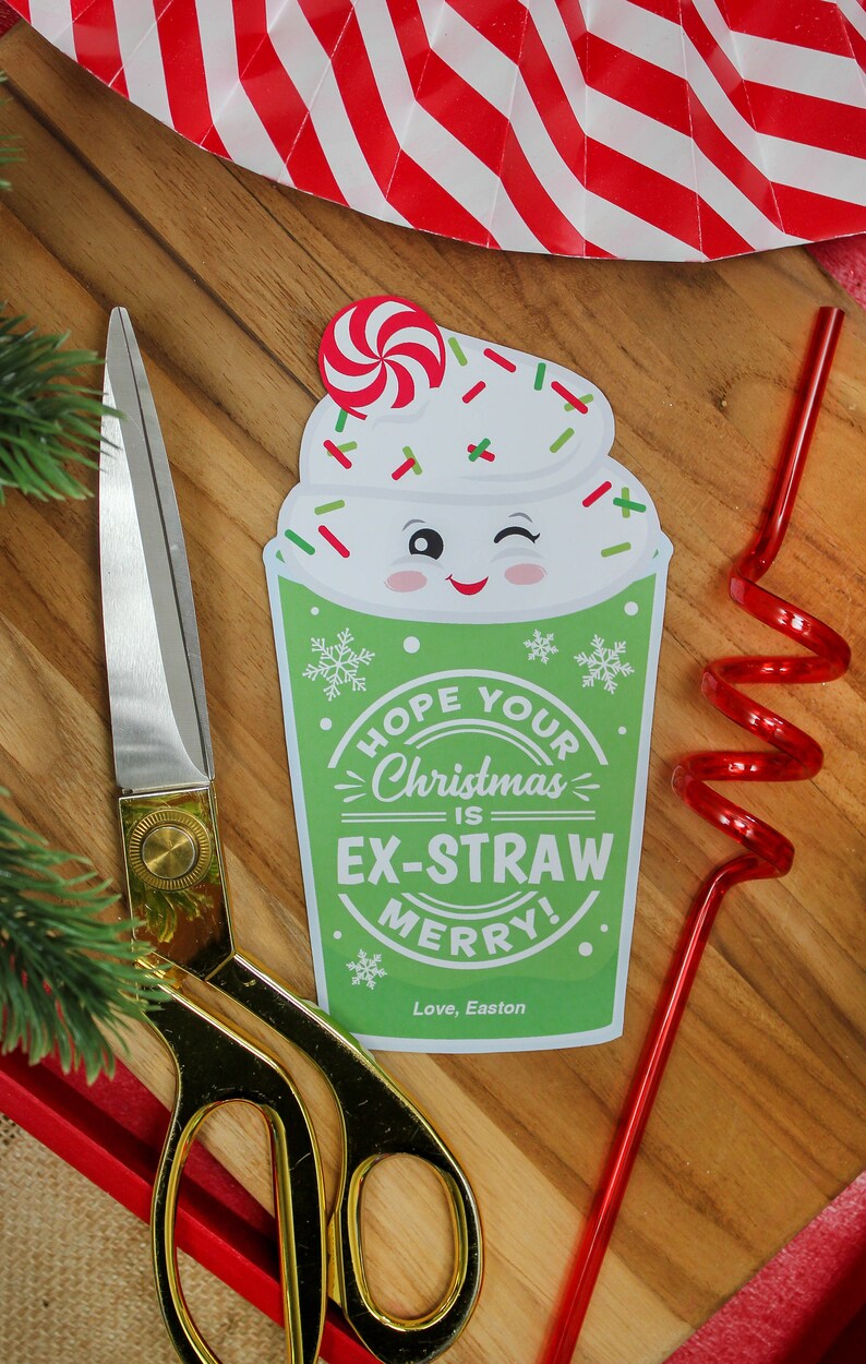 May include: A green and white Christmas-themed paper cup with a red candy cane on top. The cup has a white frosting design and a smiling face with a winking eye. The text on the cup reads "Hope your Christmas is Ex-Straw Merry! Love, Easton".