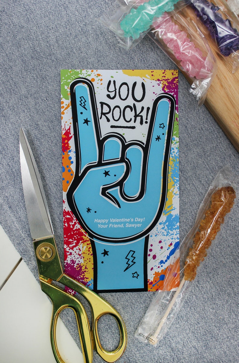 Pode incluir: Um cart&atilde;o colorido com uma m&atilde;o azul fazendo o gesto de rock and roll. O cart&atilde;o diz "You Rock!" e "Happy Valentine's Day! Your Friend, Sawyer".