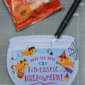 May include: A blue and white card shaped like a fishbowl with a spider hanging from the top. Inside the bowl are three cartoon fish with Halloween costumes. The text on the card reads "Hope you have a fin-tastic Halloween!" and "Happy Halloween! Love, Easton".