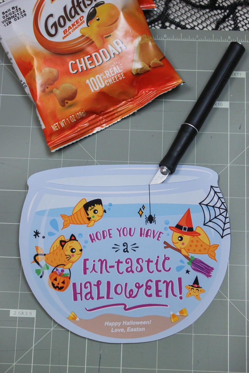 May include: A blue and white card shaped like a fishbowl with a spider hanging from the top. Inside the bowl are three cartoon fish with Halloween costumes. The text on the card reads "Hope you have a fin-tastic Halloween!" and "Happy Halloween! Love, Easton".