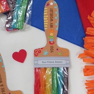 May include: A paint brush shaped gift tag with a rainbow of colorful candy sticks. The tag reads "YOU COLOR MY WORLD!" and "Your Friend, Easton". A red heart is next to the tag. Other tags and colorful paper are in the background.