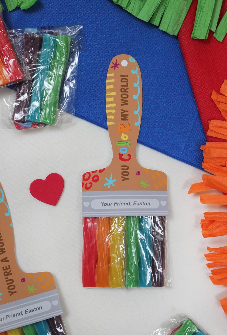 May include: A paint brush shaped gift tag with a rainbow of colorful candy sticks. The tag reads "YOU COLOR MY WORLD!" and "Your Friend, Easton". A red heart is next to the tag. Other tags and colorful paper are in the background.