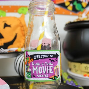 May include: A glass bottle with a yellow and white striped straw, decorated with a purple and green sticker that says "Welcome to Thrills & Chills Movie Theater".