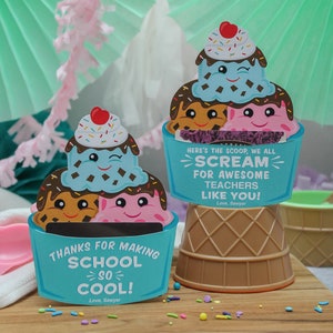 Puede incluir: Dos etiquetas de regalo con forma de cono de helado con fondo azul y un cono de helado de dibujos animados con una cara sonriente. El texto en las etiquetas dice "Gracias por hacer que la escuela sea tan genial! Con cari&ntilde;o, Sawyer" y "Aqu&iacute; est&aacute; la primicia, todos gritamos por los incre&iacute;bles maestros como t&uacute;! Con cari&ntilde;o, Sawyer".