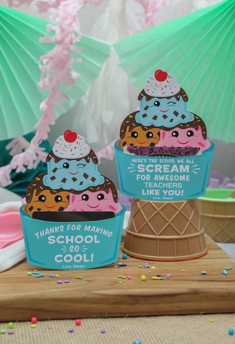 Puede incluir: Dos etiquetas de regalo con forma de cono de helado con fondo azul y un cono de helado de dibujos animados con una cara sonriente. El texto en las etiquetas dice "Gracias por hacer que la escuela sea tan genial! Con cari&ntilde;o, Sawyer" y "Aqu&iacute; est&aacute; la primicia, todos gritamos por los incre&iacute;bles maestros como t&uacute;! Con cari&ntilde;o, Sawyer".