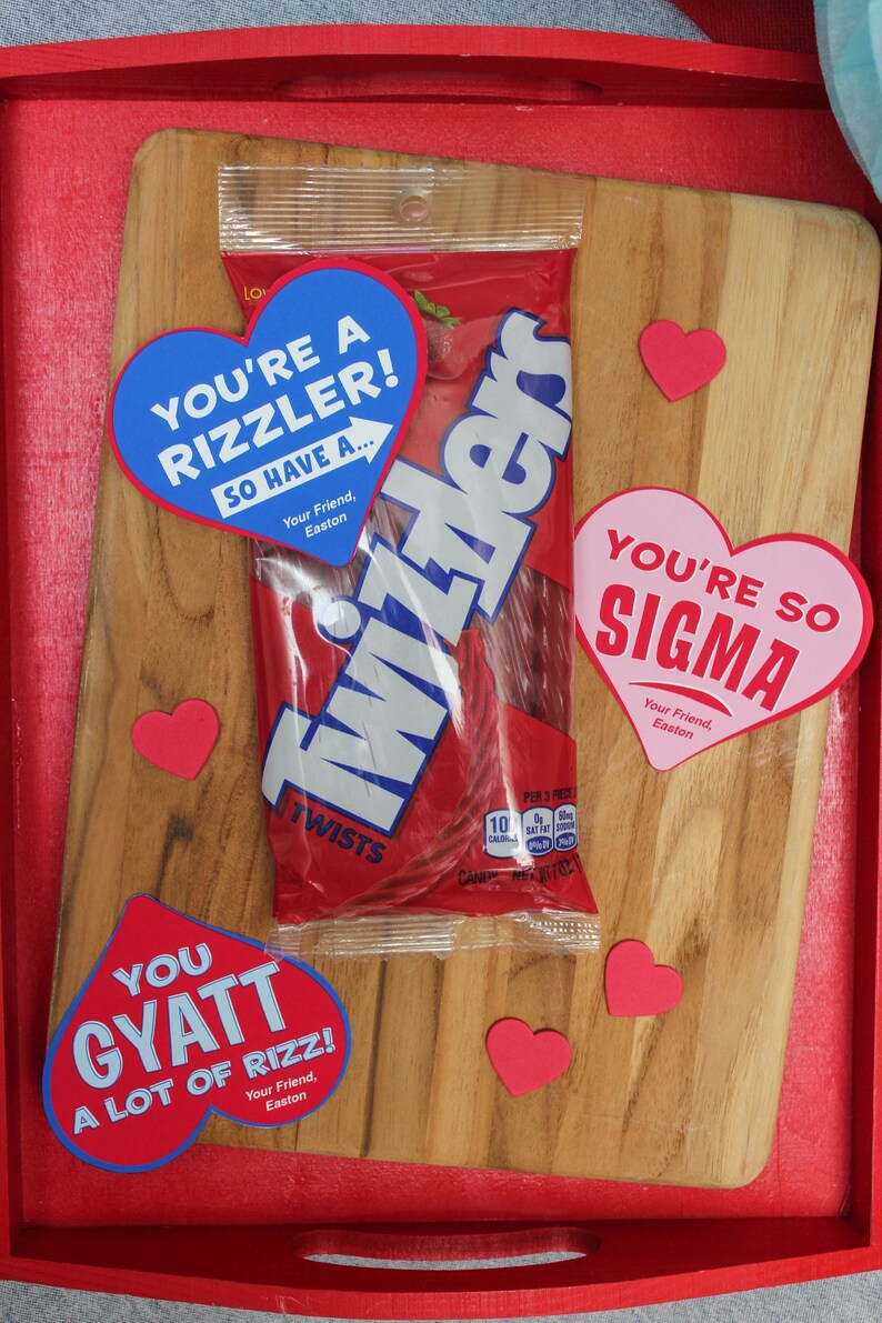 May include: A red wooden tray with a package of Twizzlers candy and several heart-shaped paper notes. The notes have different messages, including "You're a rizzler! So have a...", "You're so sigma", and "You gyatt a lot of rizz!"