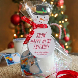K&ouml;nnte beinhalten: Ein Schneemann-Geschenk-Anh&auml;nger mit dem Text "Snow Happy We're Friends! Have a fun holiday! Love, Sawyer" ist mit einem roten Band an einem durchsichtigen Plastikbeutel gebunden, der mit wei&szlig;en Konfetti und einem Schneemann-Aufkleber gef&uuml;llt ist.