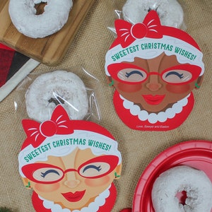 May include: Two red and white Christmas gift bags with a donut inside. The bags feature a cartoon woman with red glasses and the text "Sweetest Christmas Wishes!" and "Love, Sawyer and Easton".