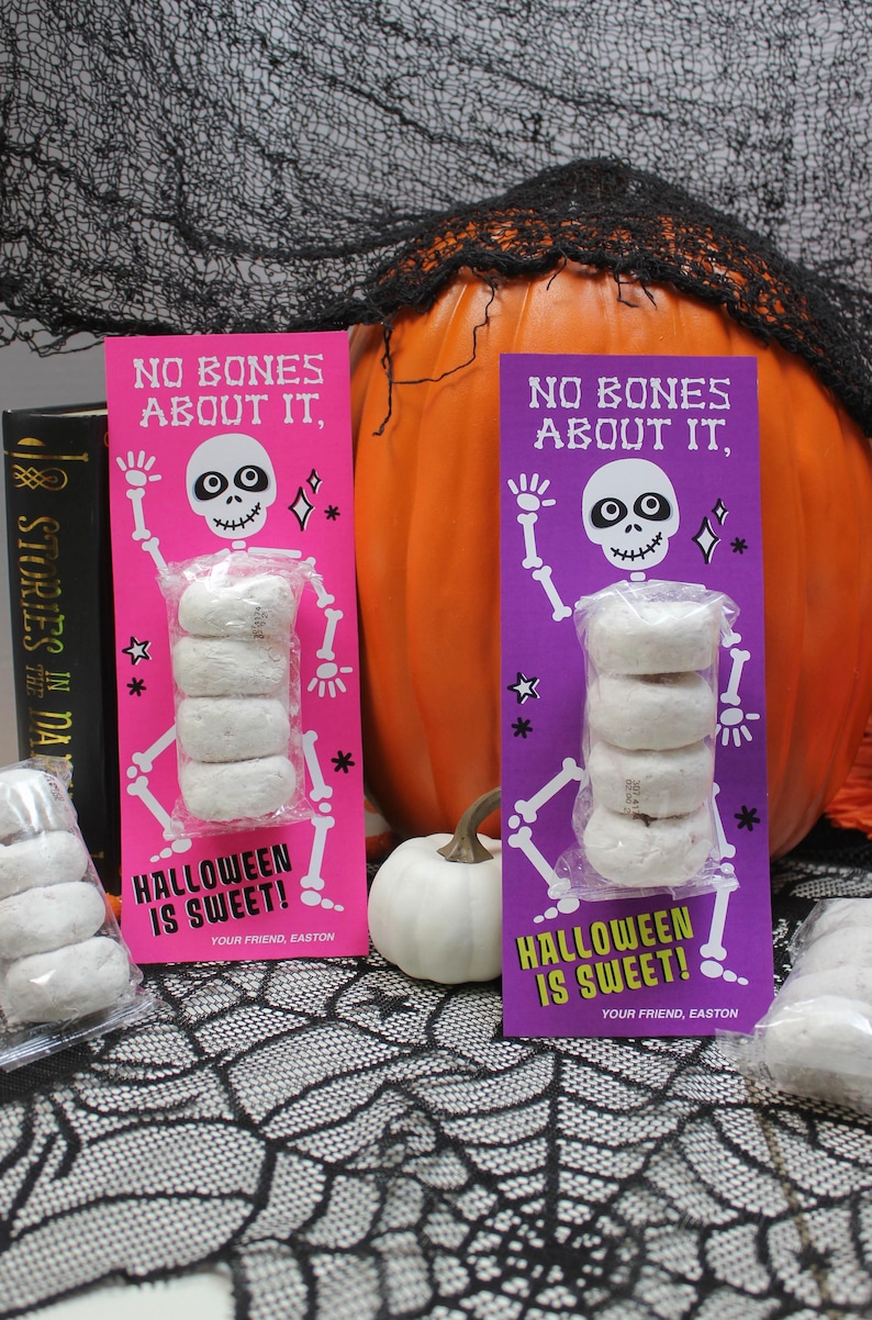 May include: Two pink and purple Halloween treat bags with donuts stacked inside. The bags feature a skeleton with the text "No bones about it, Halloween is sweet!"