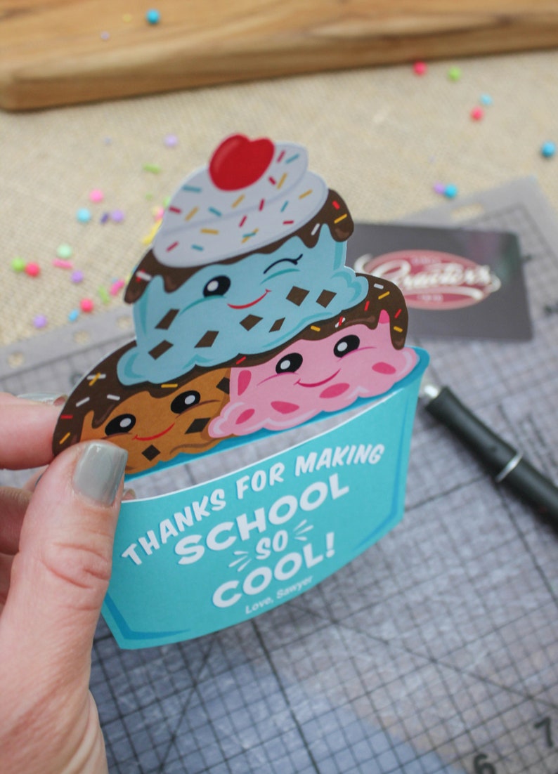 Puede incluir: Una tarjeta de cono de helado azul y blanco con una cara sonriente y el texto "Gracias por hacer la escuela tan genial! Con cari&ntilde;o, Sawyer".