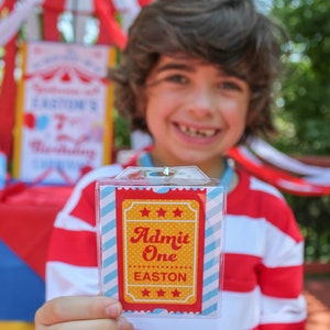 May include: A child holds a red, white, and blue striped ticket with the text "Admit One Easton" in a yellow star-shaped frame. The ticket is in a clear plastic holder.
