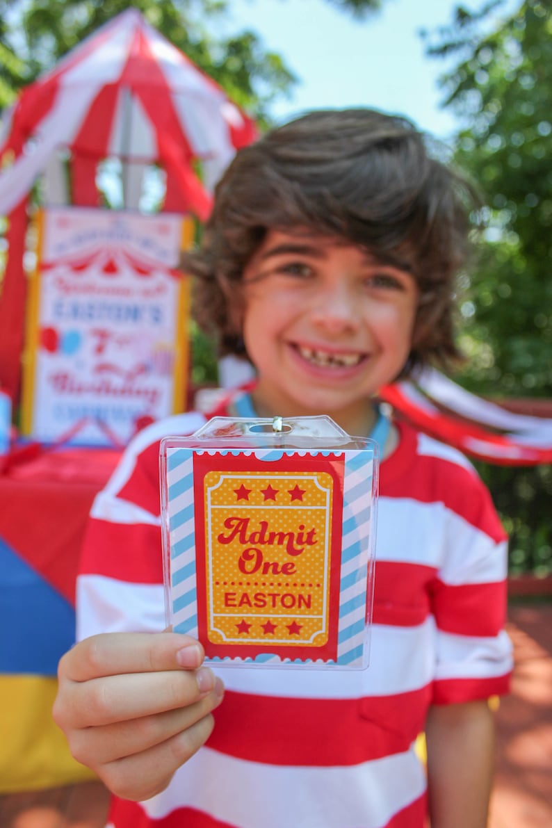 May include: A child holds a red, white, and blue striped ticket with the text "Admit One Easton" in a yellow star-shaped frame. The ticket is in a clear plastic holder.
