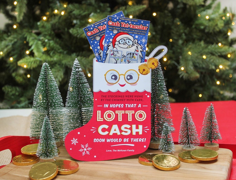 Pode incluir: Uma meia vermelha com uma borda branca e um rosto de boneco de neve est&aacute; cheia de dois bilhetes de loteria. A meia est&aacute; sobre uma superf&iacute;cie de madeira com pequenas &aacute;rvores de Natal artificiais e moedas de ouro.