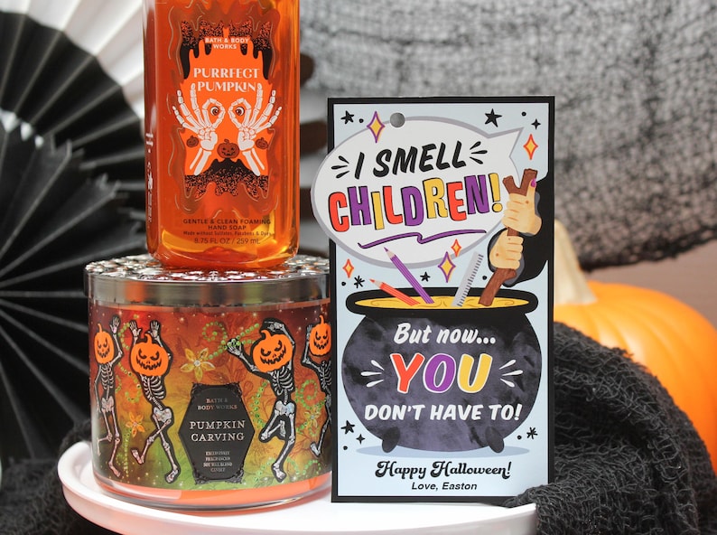 May include: A Halloween-themed candle with a pumpkin carving design and skeletons dancing. The candle is in a clear glass jar with a black lid. A card with the text "I smell children! But now... you don't have to! Happy Halloween! Love, Easton" is in the foreground.