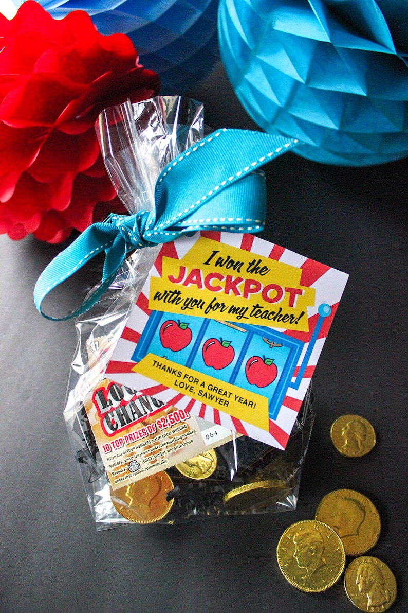 May include: A clear plastic bag tied with a blue ribbon and a red and white card that says "I won the JACKPOT with you for my teacher!"  The card has a slot machine design with three red apples. The bag contains gold chocolate coins and black shredded paper.
