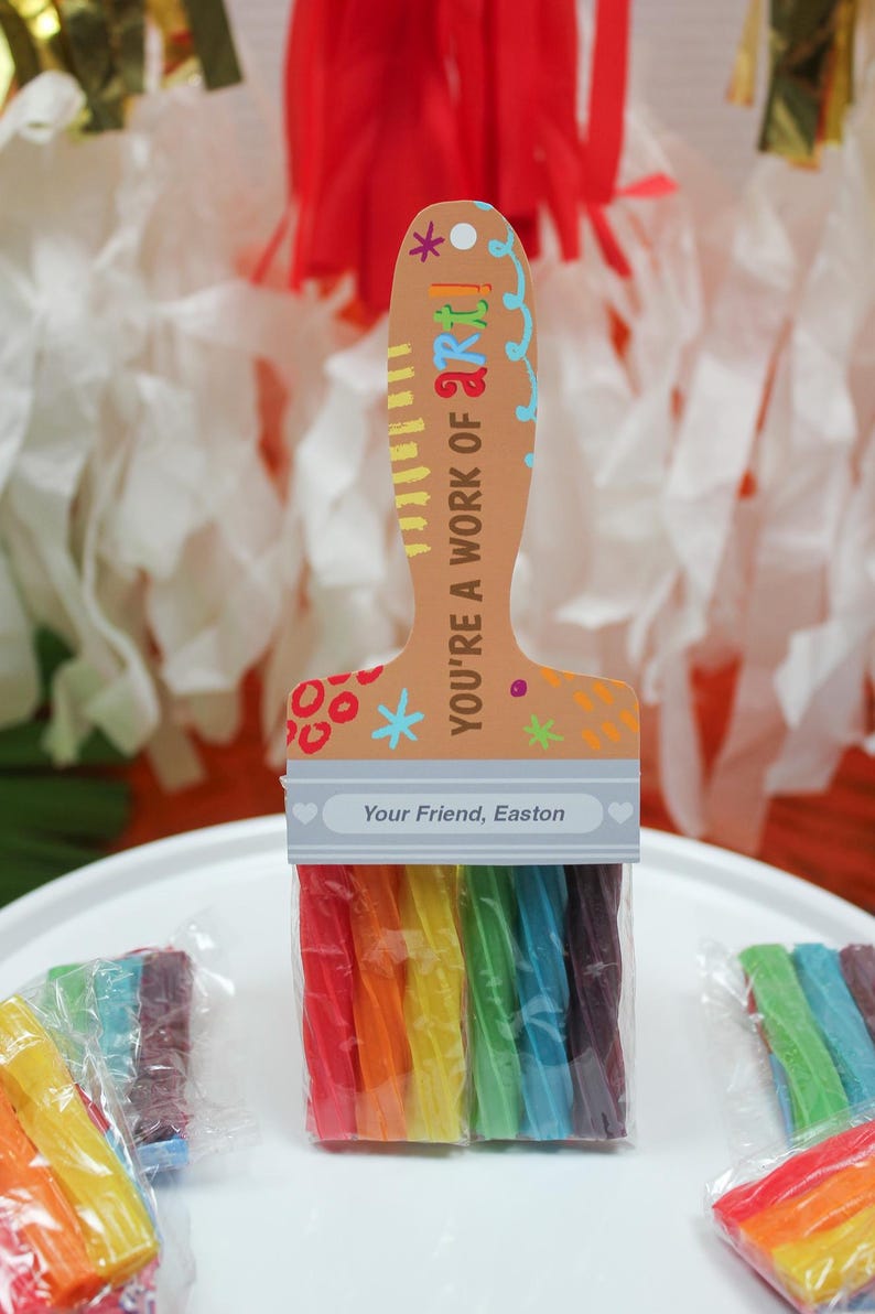 May include: A paintbrush-shaped gift with rainbow-colored candy 'bristles'. The handle is tan with the text 'YOU'RE A WORK OF ART!' and 'Your Friend, Easton'. A creative and colorful treat, perfect for art lovers.