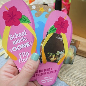 May include: Pink and yellow flip-flop shaped card with the text "School work: GONE Flip flop" and a hibiscus flower. The card is being held in a hand and has a gift card tucked inside. The gift card is for a spa and has the text "Envy Spa" on it.
