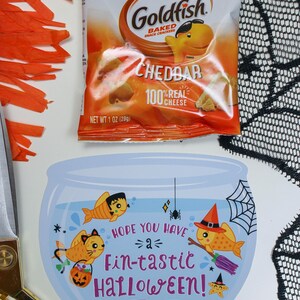 May include: A blue and white card with a goldfish bowl illustration. Three goldfish are inside the bowl, one wearing a witch's hat, one wearing a cat costume, and one wearing a Frankenstein costume. The card says "Hope you have a fin-tastic Halloween!" and "Happy Halloween! Love, Easton".