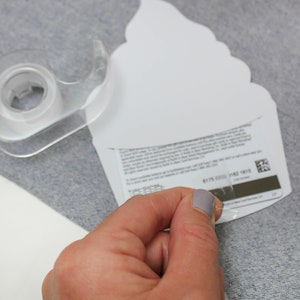 May include: A white cupcake-shaped gift card with a clear adhesive strip being peeled off. The gift card has a barcode and text on the back.