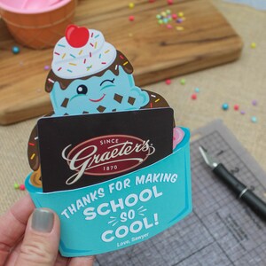 Puede incluir: Una tarjeta en forma de cono de helado azul y blanco con el texto "Gracias por hacer que la escuela sea tan genial! Con cari&ntilde;o, Sawyer". La tarjeta tiene una tarjeta de regalo de Graeter's Ice Cream en su interior.