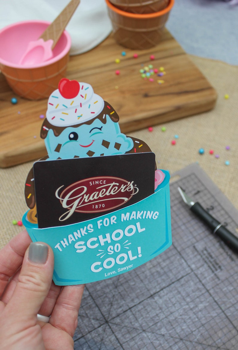 Puede incluir: Una tarjeta en forma de cono de helado azul y blanco con el texto "Gracias por hacer que la escuela sea tan genial! Con cari&ntilde;o, Sawyer". La tarjeta tiene una tarjeta de regalo de Graeter's Ice Cream en su interior.