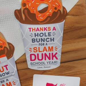 May include: A donut-shaped card with a smiling face and sprinkles, in a coffee cup with the text "Thanks a hole bunch for a slam dunk school year! Love, Sawyer". The card is next to a Dunkin' Donuts gift card.
