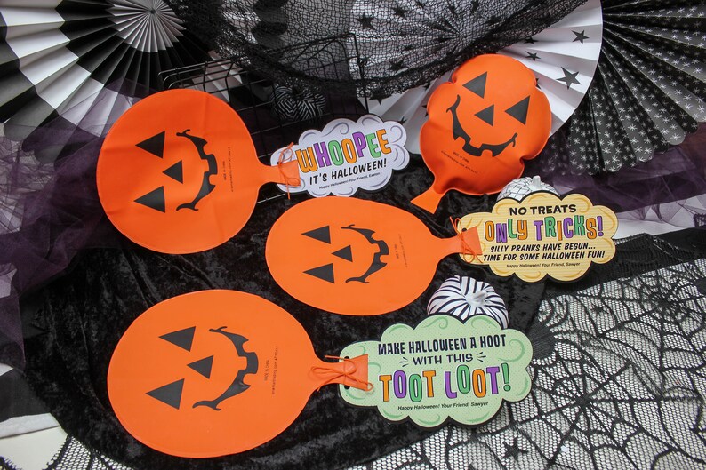 May include: Four orange Halloween trick or treat bags with jack-o-lantern faces. The bags have attached tags with Halloween-themed messages, including "Whooppee! It's Halloween!" and "No Treats Only Tricks! Silly Pranks Have Begun... Time For Some Halloween Fun!"