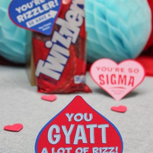 May include: Red heart-shaped card with blue text that reads "You Gyatt A Lot Of Rizz!" with the text "Your Friend, Easton" at the bottom. The card is surrounded by small red hearts.
