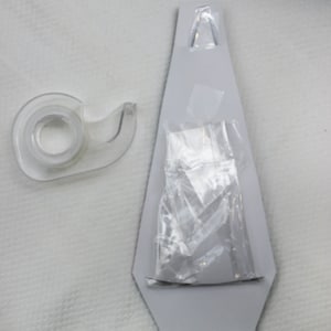 Peut inclure: Un distributeur de ruban adh&eacute;sif en plastique transparent sur fond blanc. Le ruban est partiellement d&eacute;roul&eacute; et il y a un sac en plastique transparent avec une &eacute;tiquette blanche &agrave; l'int&eacute;rieur d'une d&eacute;coupe en carton gris d'une lampe &agrave; lave.