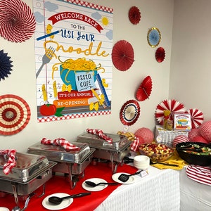 May include: A red and white checkered tablecloth covers a buffet table with three silver chafing dishes. The table is decorated with red and white paper fans. A sign above the table reads "Welcome Back to the Use Your Noodle Pasta Cafe. It's Our Annual Re-Opening!"