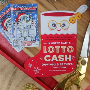 Pode incluir: Uma meia vermelha com uma borda branca e um rosto sorridente com &oacute;culos. A meia tem um sino dourado de cada lado e o texto "In hopes that a Lotto Cash soon would be there! Love, The McKown Family".