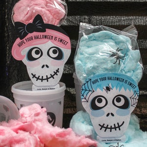 Puede incluir: Dos recipientes de algod&oacute;n de az&uacute;car con tapas en forma de calavera. Las tapas est&aacute;n decoradas con telara&ntilde;as y el texto "HOPE YOUR HALLOWEEN IS SWEET". Los recipientes est&aacute;n etiquetados con "Love, Sawyer & Easton".