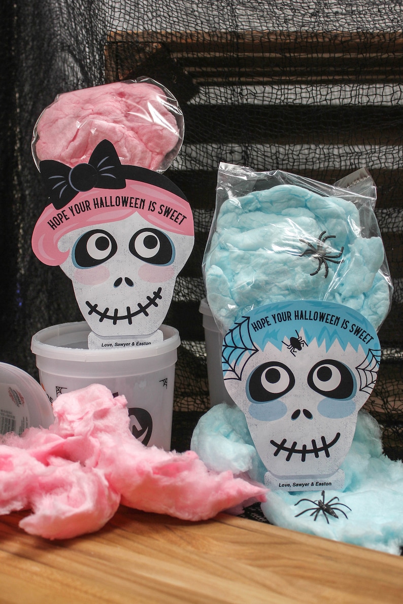 Puede incluir: Dos recipientes de algod&oacute;n de az&uacute;car con tapas en forma de calavera. Las tapas est&aacute;n decoradas con telara&ntilde;as y el texto "HOPE YOUR HALLOWEEN IS SWEET". Los recipientes est&aacute;n etiquetados con "Love, Sawyer & Easton".