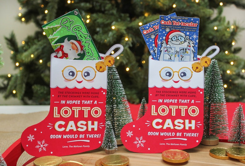 Pode incluir: Dois cart&otilde;es de Natal em forma de meia vermelha e branca com um rosto sorridente, &oacute;culos e sinos. Cada cart&atilde;o tem o texto "Na esperan&ccedil;a de que um Lotto Cash chegue em breve!" e um bilhete de loteria dentro.