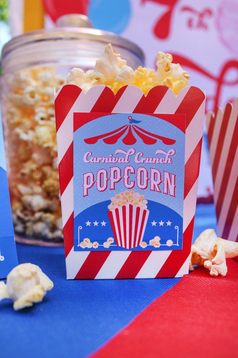 May include: Red and white striped popcorn box with a blue and red circus tent design. The box has a label that says "Carnival Crunch Popcorn".