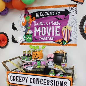 May include: A Halloween-themed party cart with a sign that reads "Creepy Concessions". The cart is decorated with black and orange balloons, a spider web, and a sign that says "Welcome to Thrills & Chills Movie Theater".