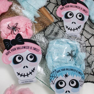 Puede incluir: Cuatro bolsas de algod&oacute;n de az&uacute;car rosa y azul con una etiqueta en forma de calavera unida a cada bolsa. Las etiquetas tienen un lazo negro, una ara&ntilde;a y el texto "Espero que tu Halloween sea dulce".