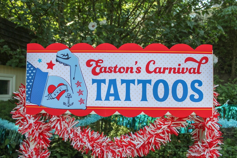May include: A red, white, and blue sign with a scalloped edge reads "Easton's Carnival Tattoos". A blue cartoon arm with a heart tattoo and an anchor tattoo is on the left side of the sign.