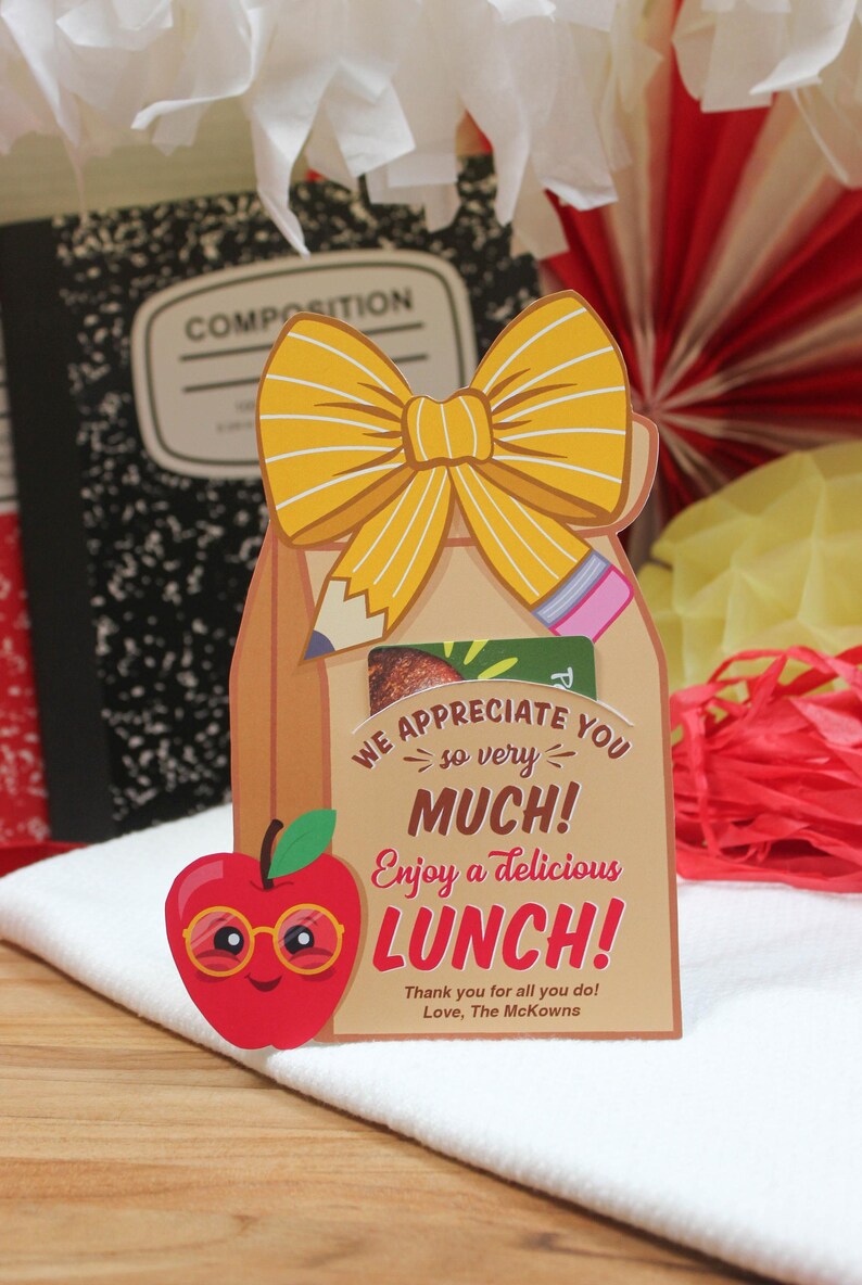 May include: A brown paper bag with a yellow bow, a red apple with googly eyes and glasses, and the text "WE APPRECIATE YOU so very MUCH! Enjoy a delicious LUNCH! Thank you for all you do! Love, The McKowns".