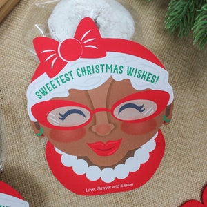 May include: A red and white Christmas gift bag featuring a cartoon illustration of a woman wearing red glasses and a red bow. The bag reads "Sweetest Christmas Wishes!" and "Love, Sawyer and Easton".