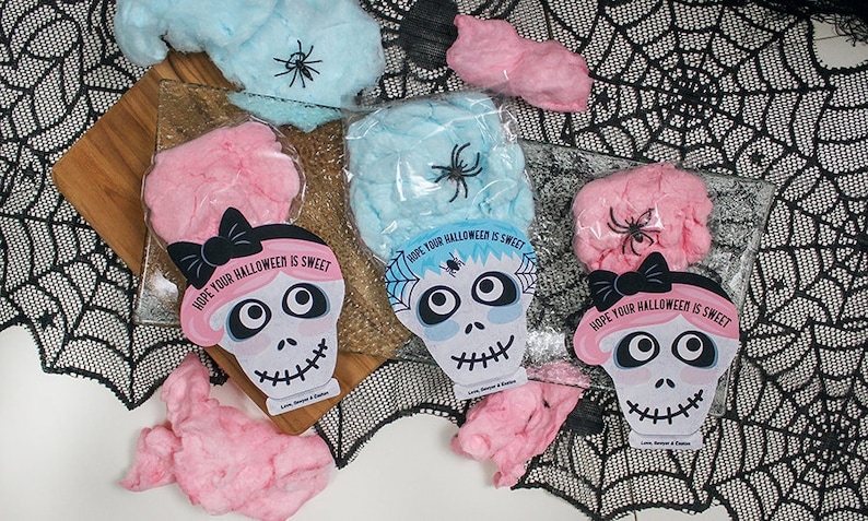 Puede incluir: Tres bolsas de algod&oacute;n de az&uacute;car rosa y azul con una tarjeta en forma de calavera unida a cada bolsa. Las tarjetas tienen un lazo negro y el texto "HOPE YOUR HALLOWEEN IS SWEET".