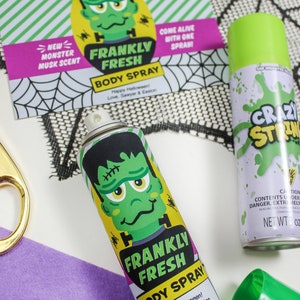 May include: Two green and white spray bottles with a monster design. The bottles are labelled "Frankly Fresh Body Spray" and "Crazy Strong". The bottles are on a black and white spiderweb pattern background.