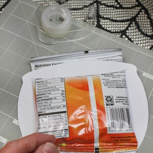 May include: A close-up of a bag of chips with a nutrition facts label. The label lists the total fat, saturated fat, trans fat, polyunsaturated fat, monounsaturated fat, cholesterol, sodium, total carbohydrate, dietary fiber, total sugars, and protein per serving. The bag is on a white surface.