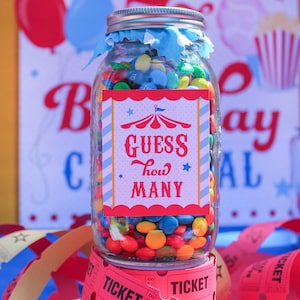 May include: A glass jar filled with colorful candy, with a red, white, and blue circus-themed label that says "Guess how many". The jar is sitting on top of a stack of red paper tickets that say "Ticket" and "Keep this coupon".