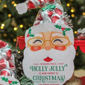 May include: A white Santa Claus face with a red hat and a green holly sprig. The Santa face has a red nose, rosy cheeks, and a white beard. The text "Wishing you a Holly Jolly and Sweet Christmas! Love, Sawyer and Easton" is printed below the Santa face.