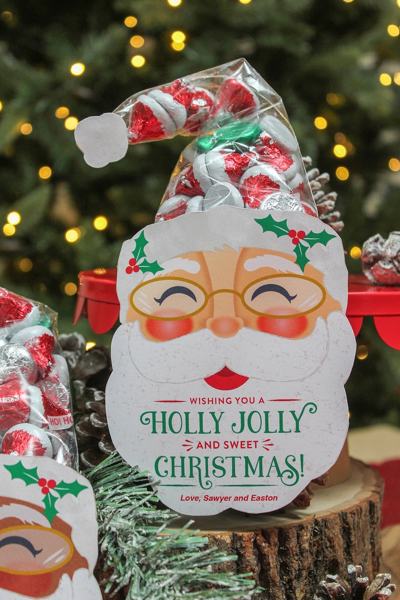 May include: A white Santa Claus face with a red hat and a green holly sprig. The Santa face has a red nose, rosy cheeks, and a white beard. The text "Wishing you a Holly Jolly and Sweet Christmas! Love, Sawyer and Easton" is printed below the Santa face.