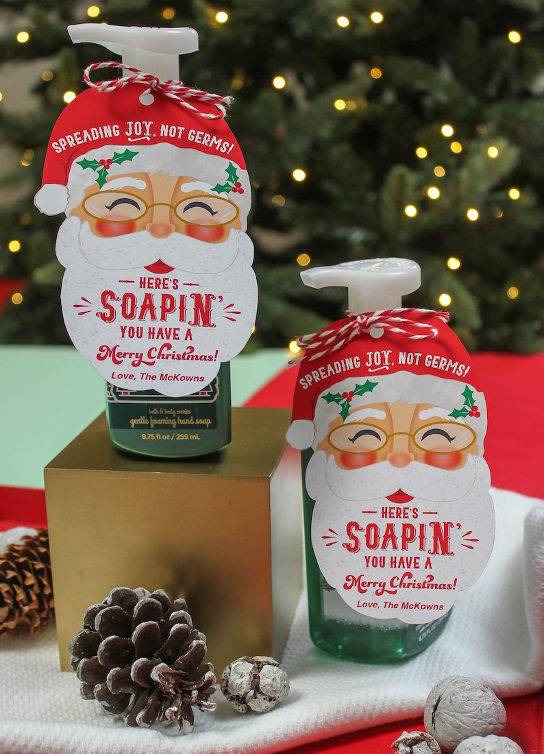 Op de afbeelding: Twee groene vloeibare zeepflessen met witte pompen en rode en witte kerstman-cadeautjes met de tekst "Spreading Joy, Not Germs!" en "Here's Soapin' You Have a Merry Christmas! Love, The McKowns".