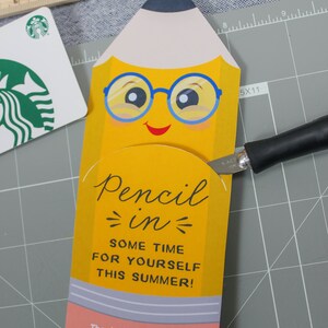 May include: A yellow pencil-shaped gift card holder with a smiling face and blue glasses. The text "Pencil in some time for yourself this summer!" is displayed. A Starbucks gift card and ruler are also visible.