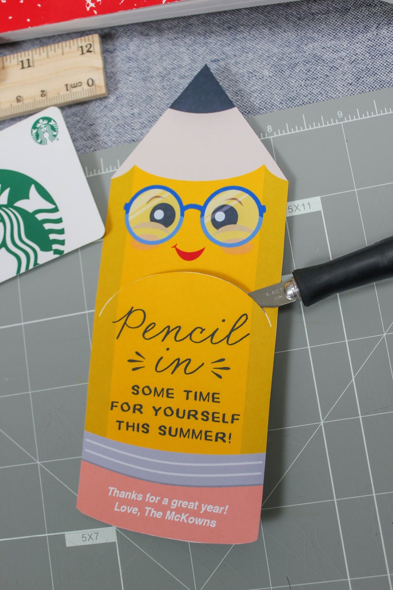 May include: A yellow pencil-shaped gift card holder with a smiling face and blue glasses. The text "Pencil in some time for yourself this summer!" is displayed. A Starbucks gift card and ruler are also visible.