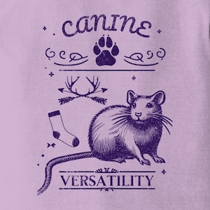 May include: A purple t-shirt with a graphic design of a rat, a paw print, antlers, a sock, and the text "canine versatility".